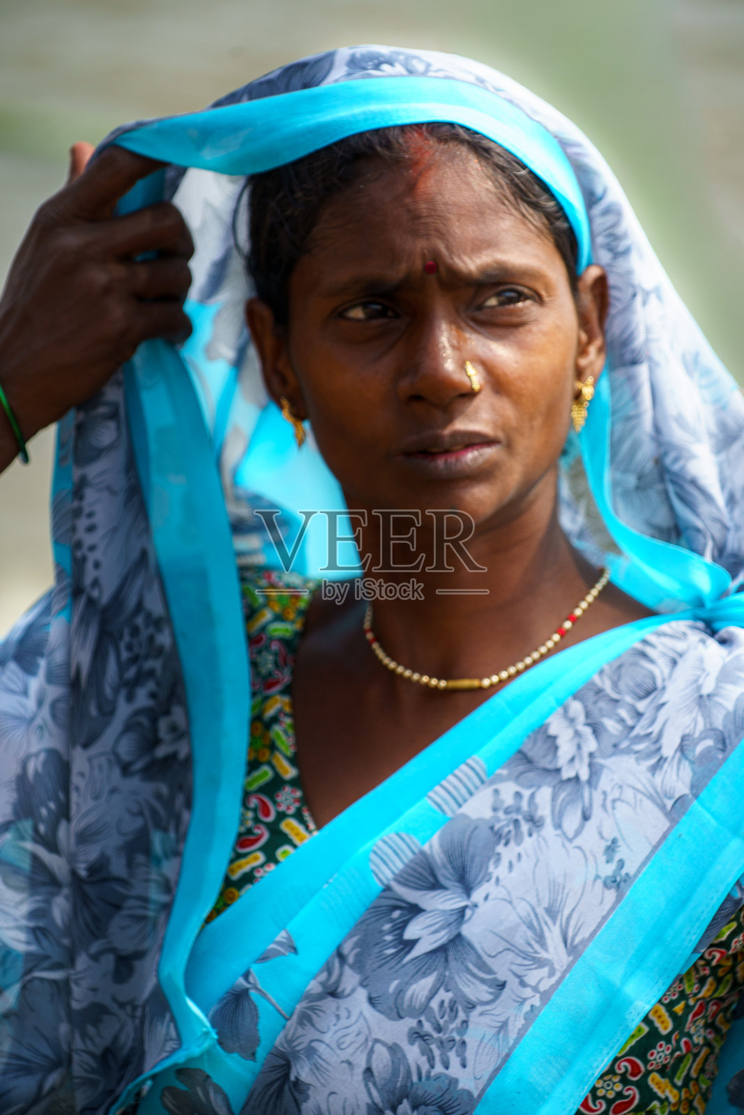 印度。北方邦。瓦拉纳西（贝拿勒斯）。一位年轻女子身着鲜艳的蓝灰色纱丽，正在调整她的头巾（dupata或pallu）的肖像。照片摄影图片