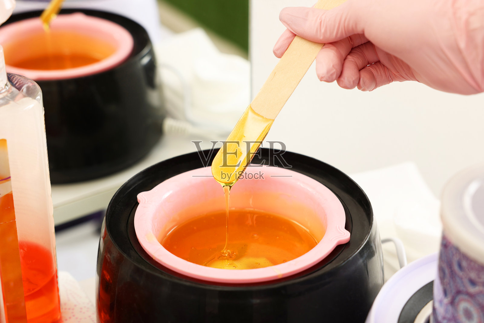 美容院里，专业美容师手持刮刀，在加热器上方展示着脱毛热蜡，特写镜头照片摄影图片