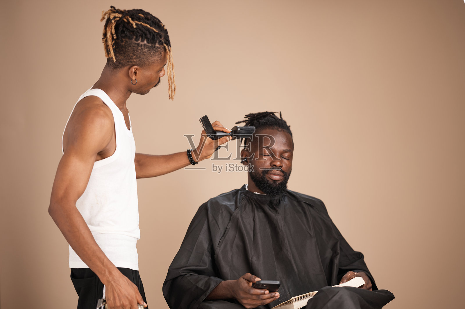 年轻的非洲理发师在工作室里为坐着的顾客理发照片摄影图片