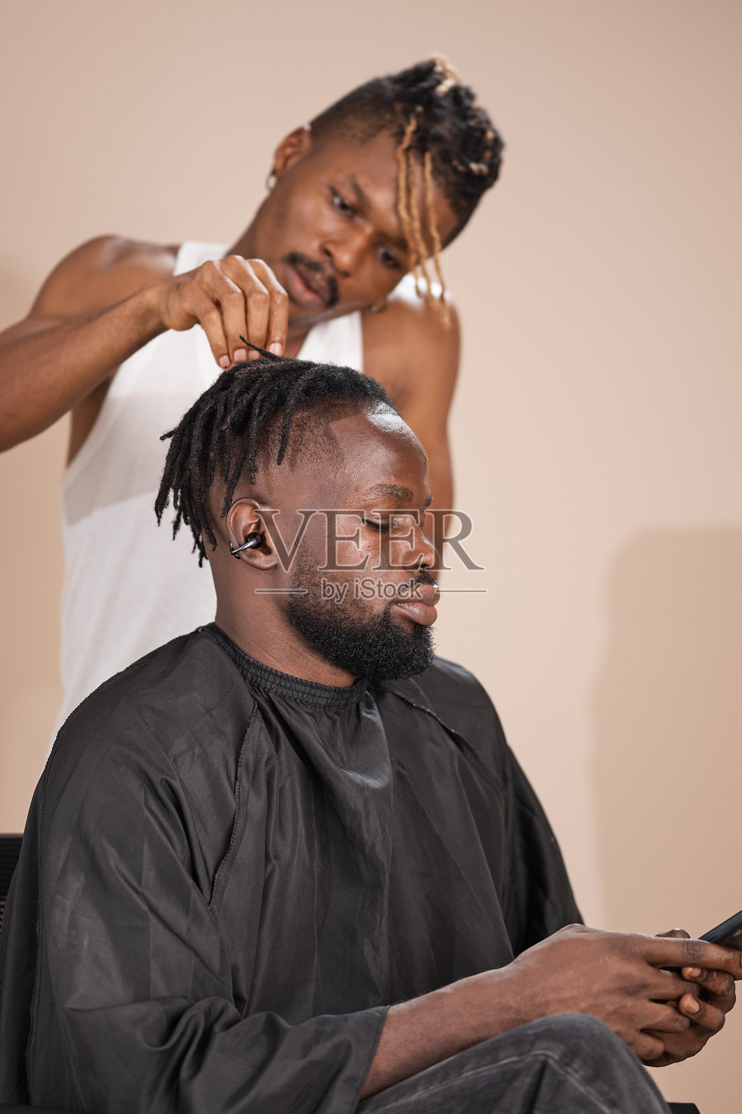 年轻的非洲理发师正在为坐着的男顾客打理脏辫照片摄影图片
