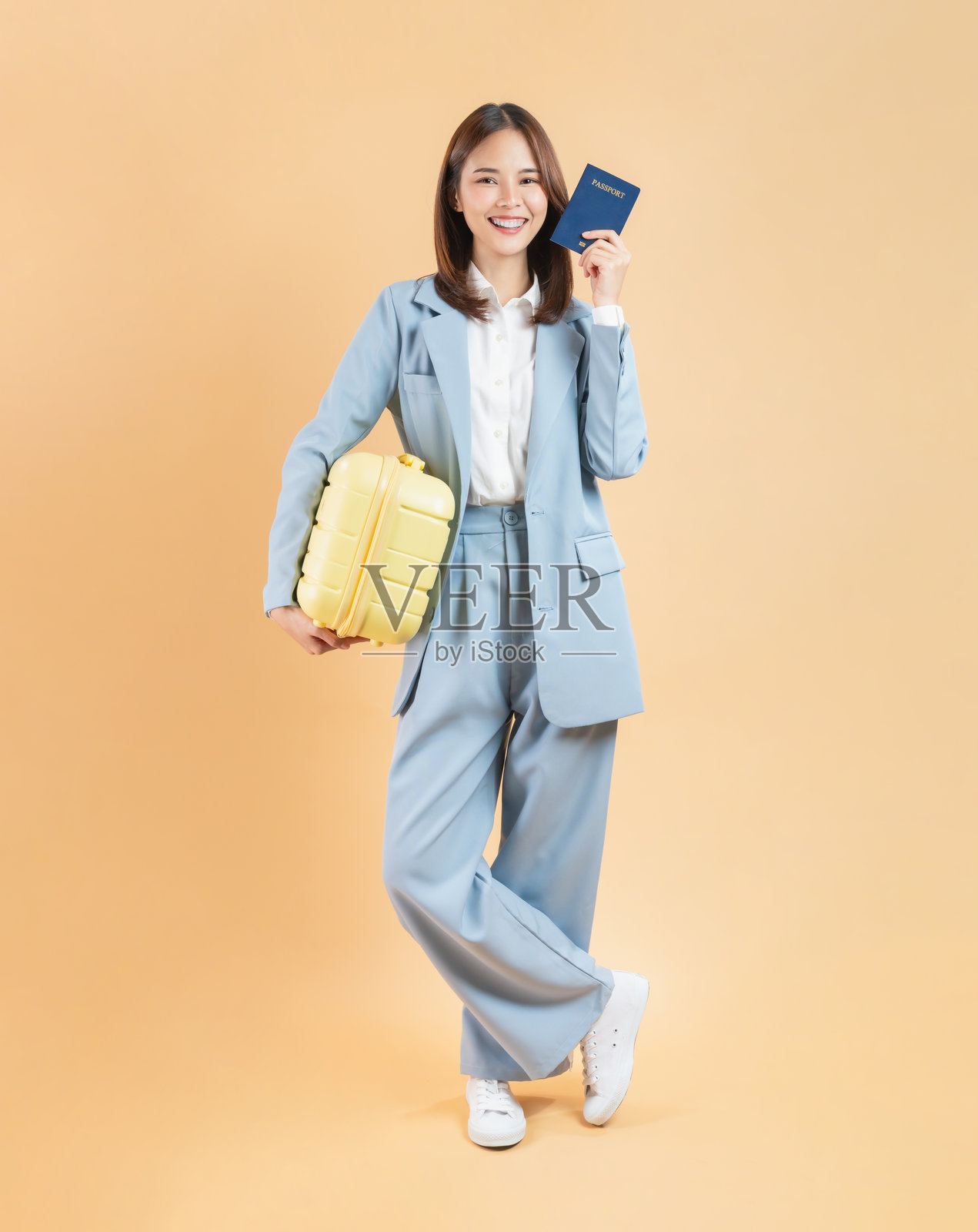 快乐的亚洲女商人，在米色背景下拿着行李箱和护照。旅游出行概念。照片摄影图片