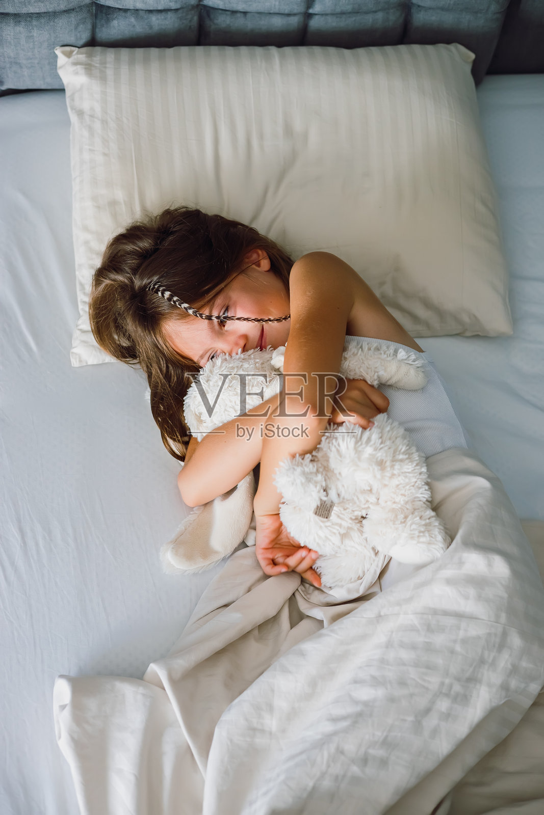 俯视视角，一个小女孩躺在舒适的床上，温柔地笑着，怀里抱着一个大大的、柔软的毛绒兔子玩具照片摄影图片