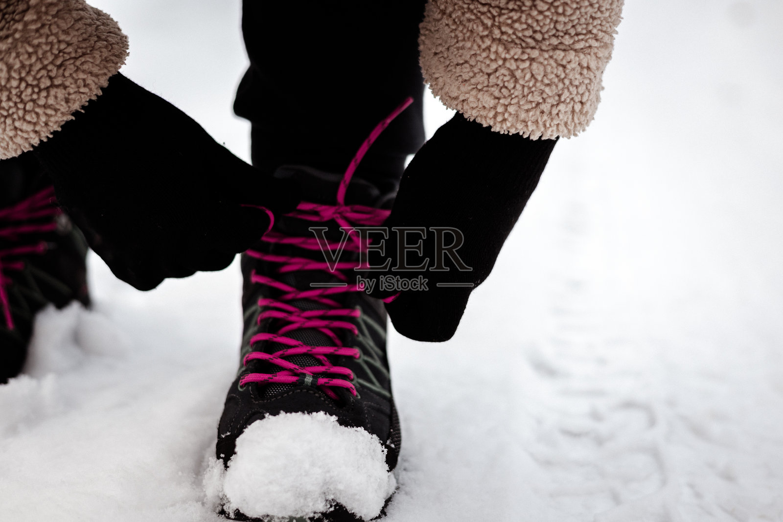 特写镜头，拍摄一只手在雪地里为黑色登山靴系粉色鞋带。真实的画面捕捉到冬季户外探险的准备过程，非常适合生活方式和运动主题的设计。照片摄影图片