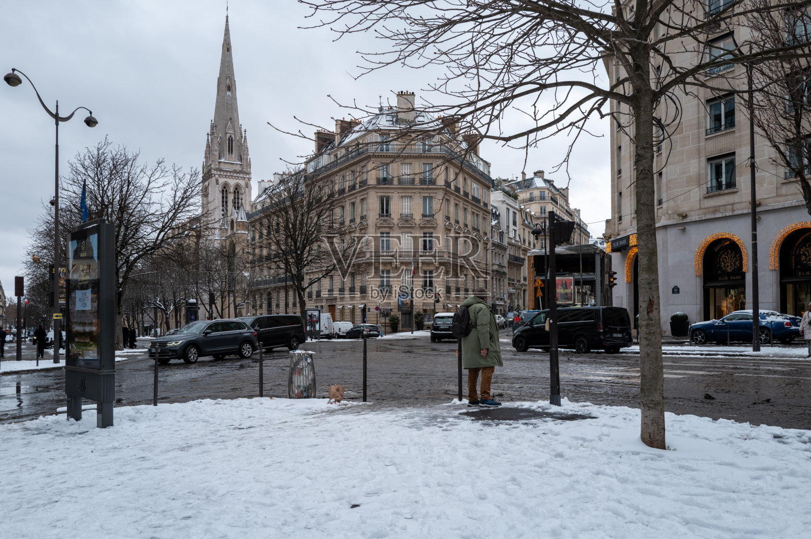 法国巴黎乔治五世大道上，覆盖着雪的街道交叉口，有行人，远处是教堂尖塔。照片摄影图片