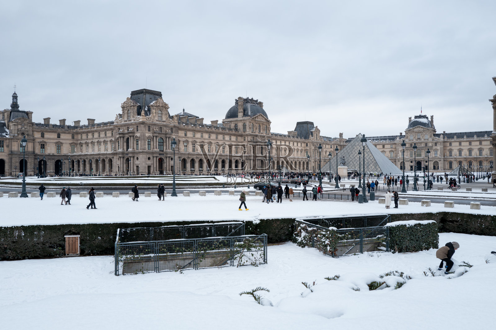 人们漫步在巴黎卢浮宫博物馆和玻璃金字塔附近的雪景庭院中，法国。照片摄影图片