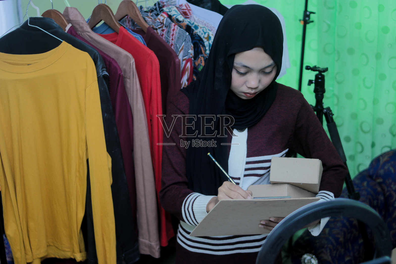 年轻的亚洲穆斯林女性在接听电话时记笔记，为她的在线服装业务工作照片摄影图片
