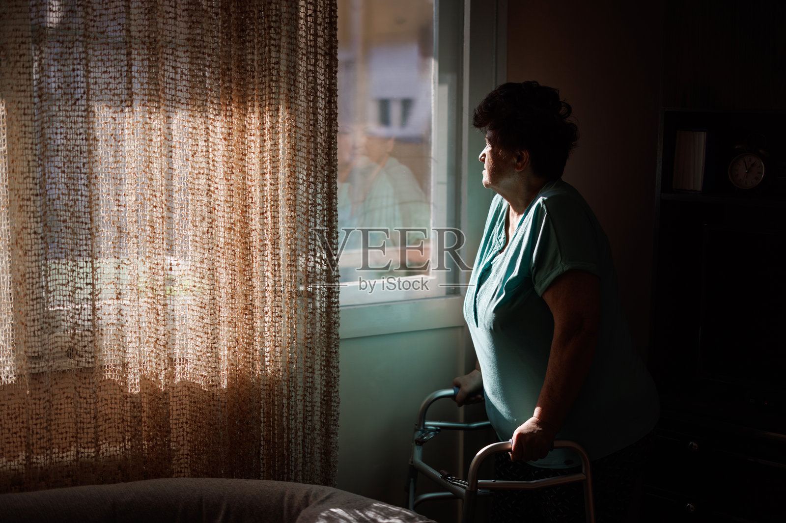 阳光下，一位拄着助行器的年长女性正望着窗外，若有所思地思考人生照片摄影图片