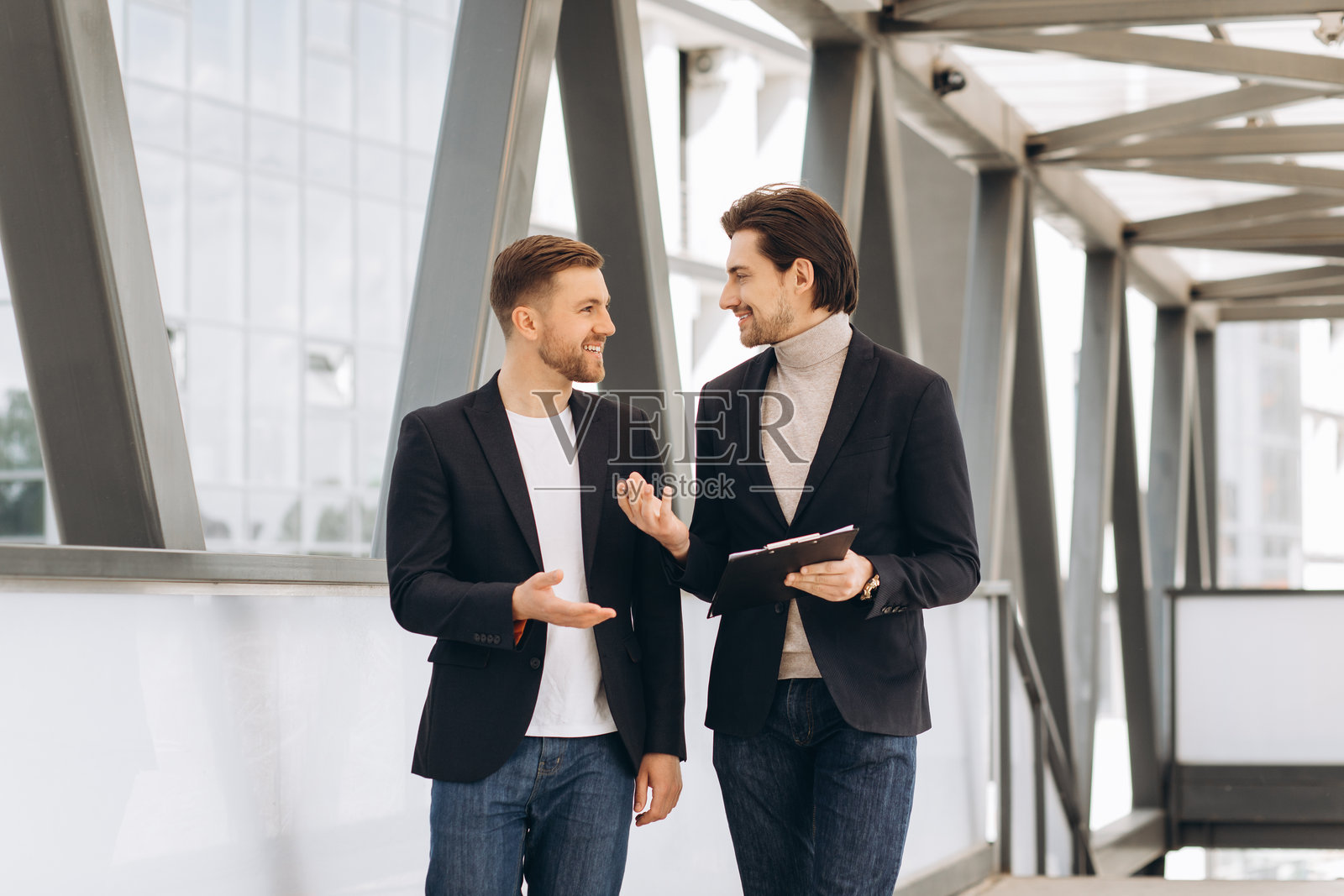 商务人士在现代玻璃走廊中边走边讨论项目，合作构思专业伙伴关系照片摄影图片