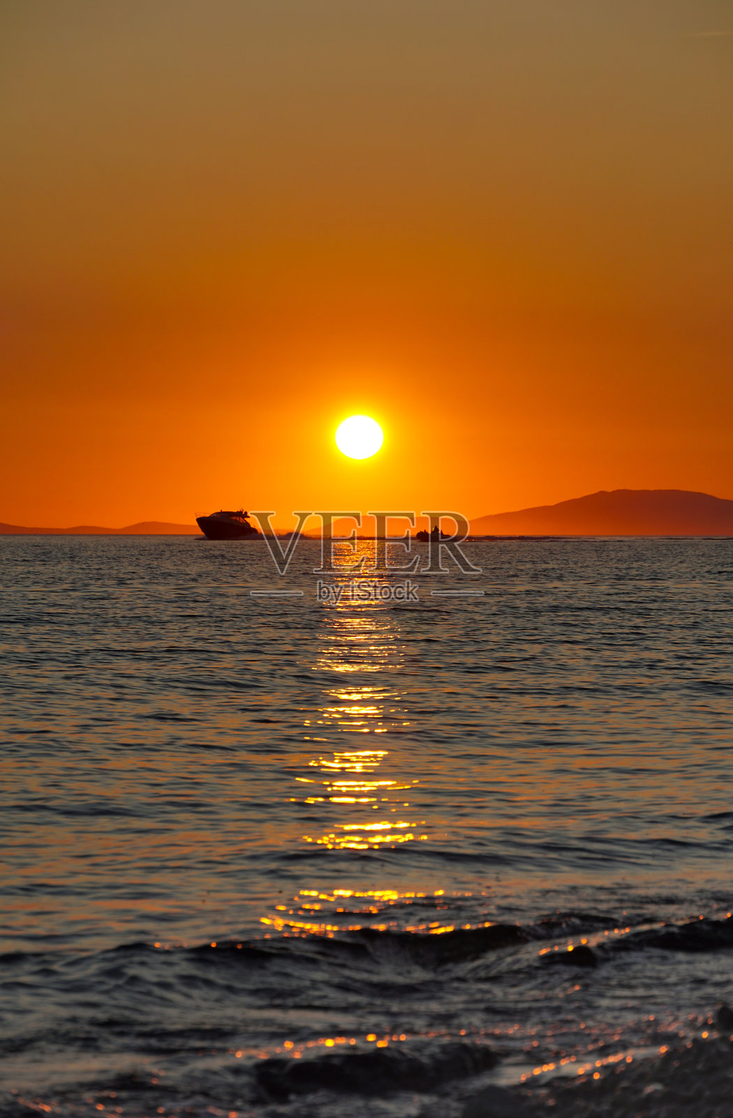 夕阳下，海面上有船只漂流的剪影，海天相接照片摄影图片