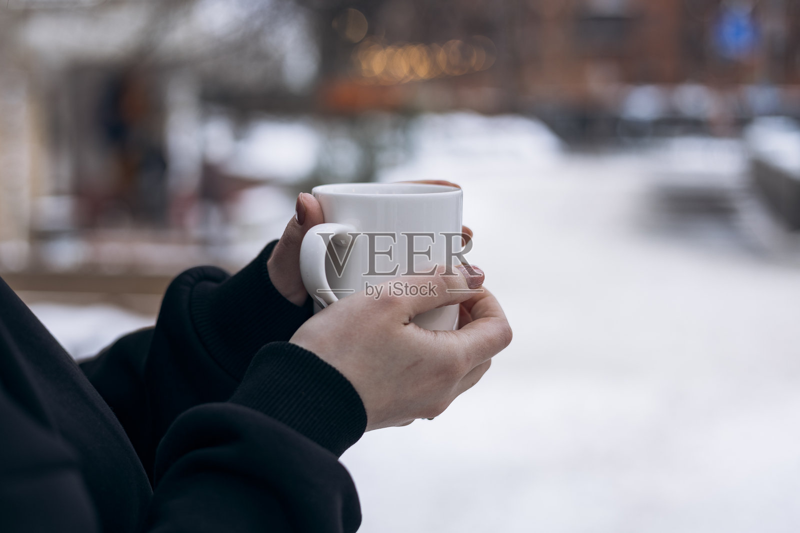手中咖啡杯，背景虚化为冬日景象，生活方式。手中咖啡杯的特写，背景虚化为冬日景象。暖饮，舒适的日常瞬间，用于广告、品牌和现代视觉内容的商业生活方式概念。照片摄影图片