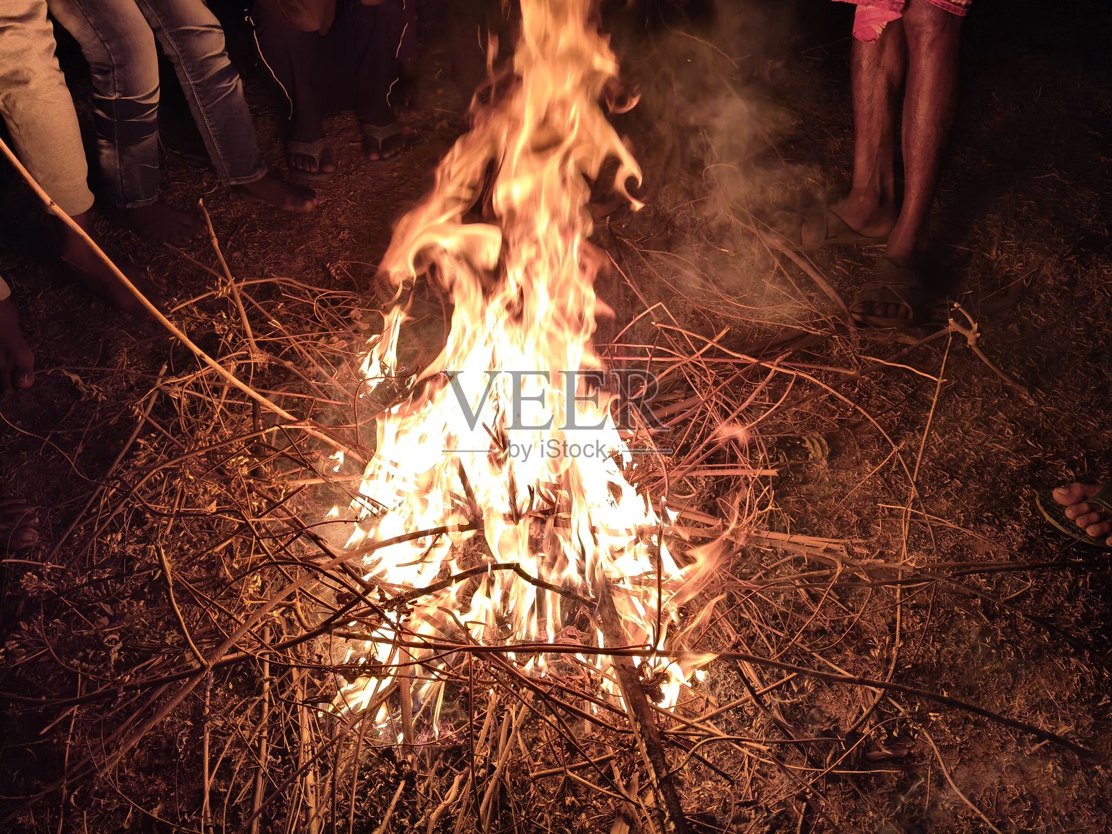 人们围坐在篝火旁，用温暖的手和脚取暖。照片摄影图片