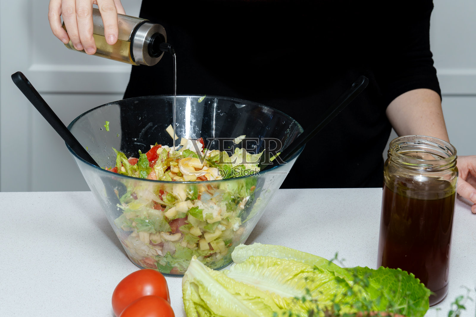 一个人正在将橄榄油淋在新鲜的绿色沙拉上照片摄影图片