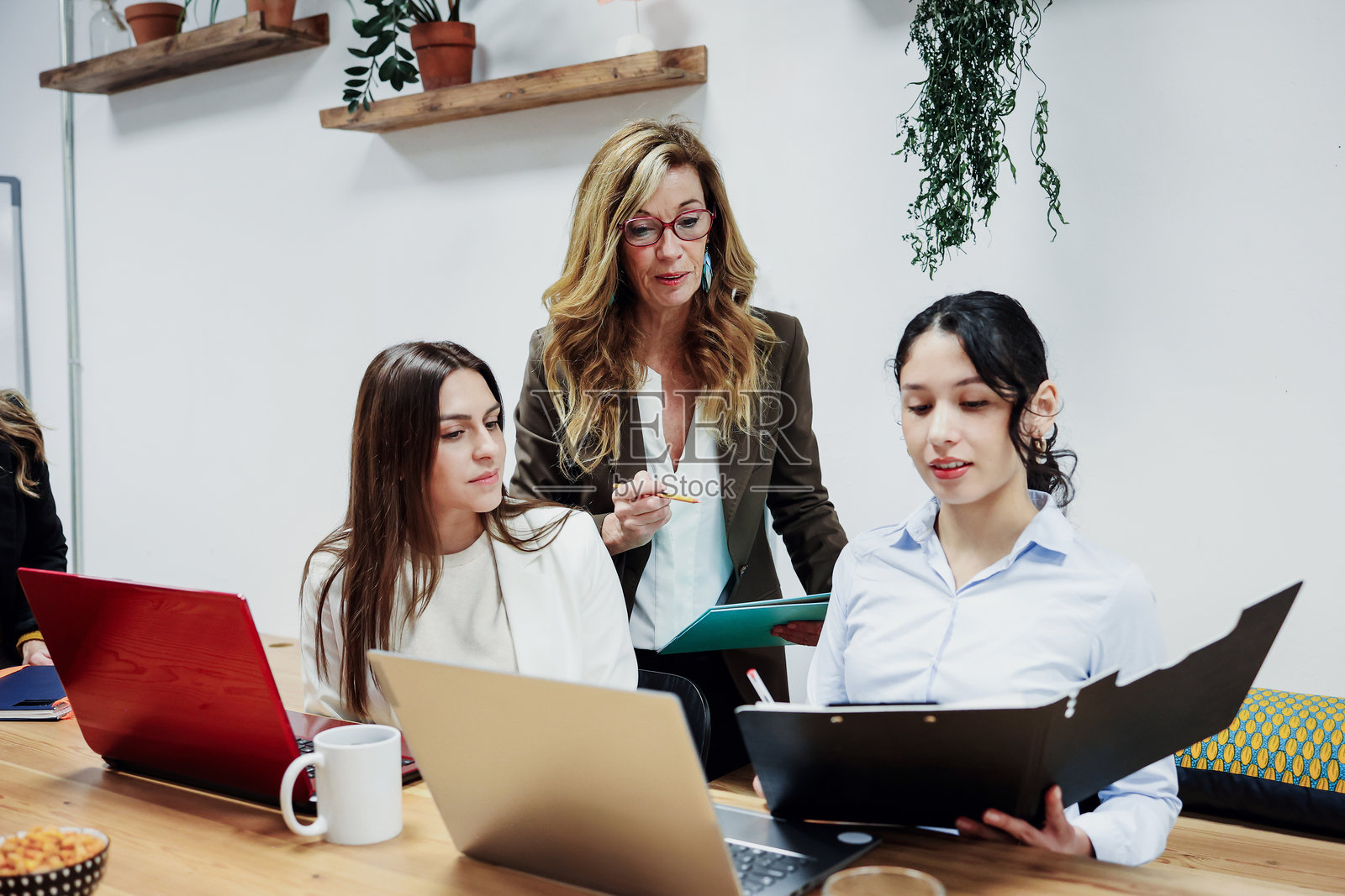 一位西班牙裔的资深女经理，在办公室或室内工作场所，与年轻的女员工和创业者一起协作，使用笔记本电脑，体现领导力概念。照片摄影图片