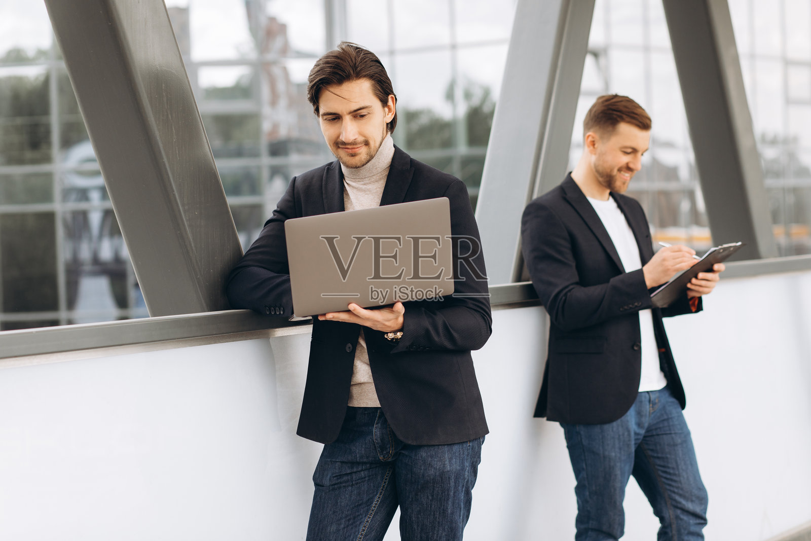 商务人士在户外合作项目，一人使用笔记本电脑，另一人写笔记，展现专业团队合作的成功照片摄影图片