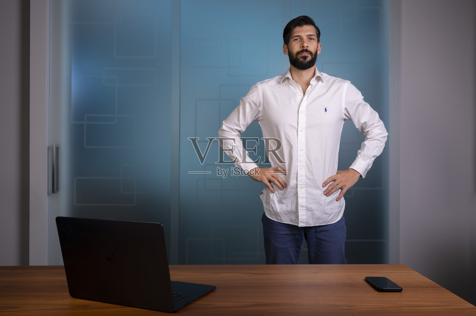 身穿白衬衫和蓝色裤子的男士站在现代办公室，代表公司业务照片摄影图片