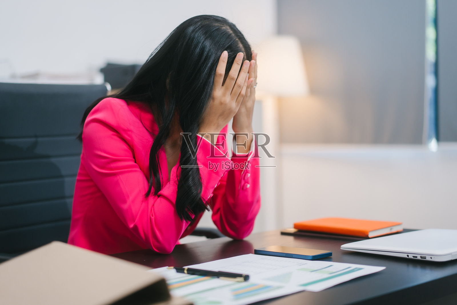 一位亚洲女商人坐在办公桌前，显得压力重重、疲惫不堪。由于长时间工作和办公室综合征，她正遭受头痛、偏头痛、颈肩疼痛和手部麻木的折磨。照片摄影图片