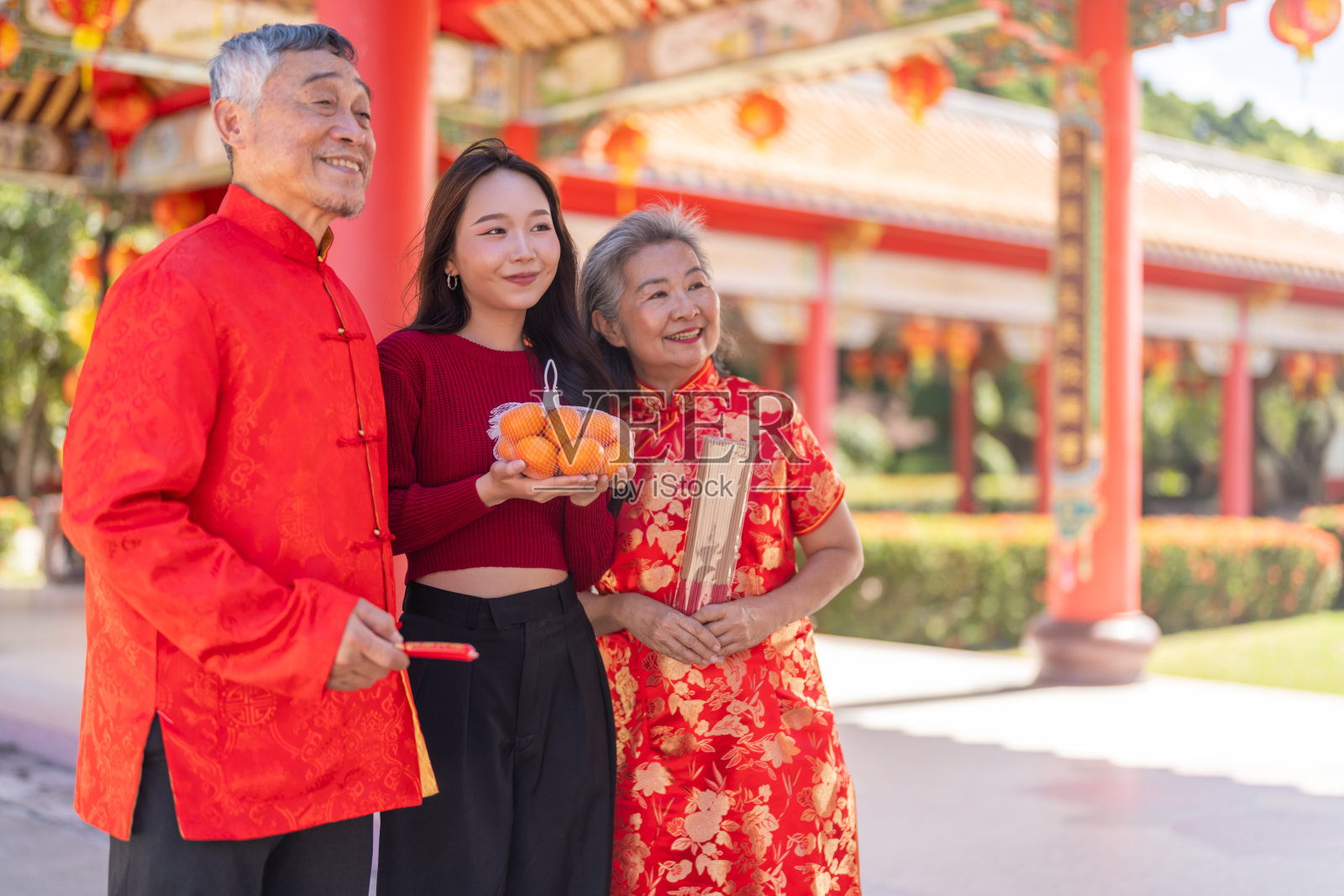 喜庆的亚洲家庭在寺庙庆祝中国新年，年长的父母和女儿穿着红色旗袍，手持橘子和香，象征农历新年的好运、节日和祈祷照片摄影图片