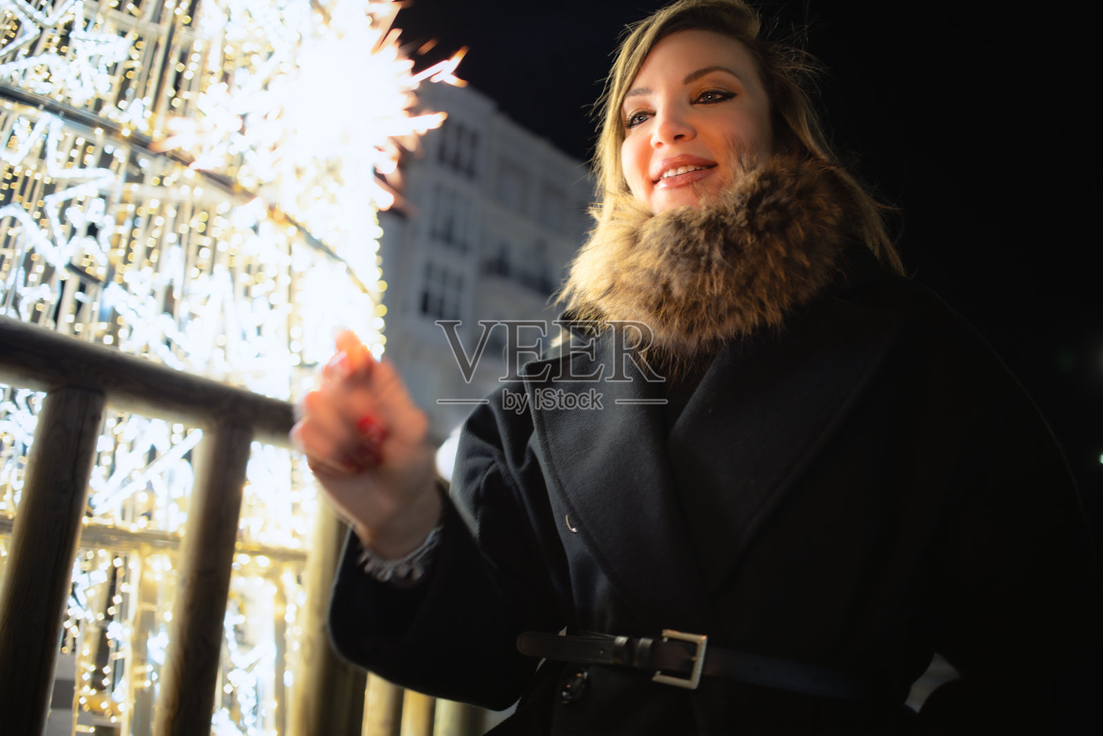 圣诞假日期间，一位女士手持仙女棒，脸上带着灿烂的笑容照片摄影图片