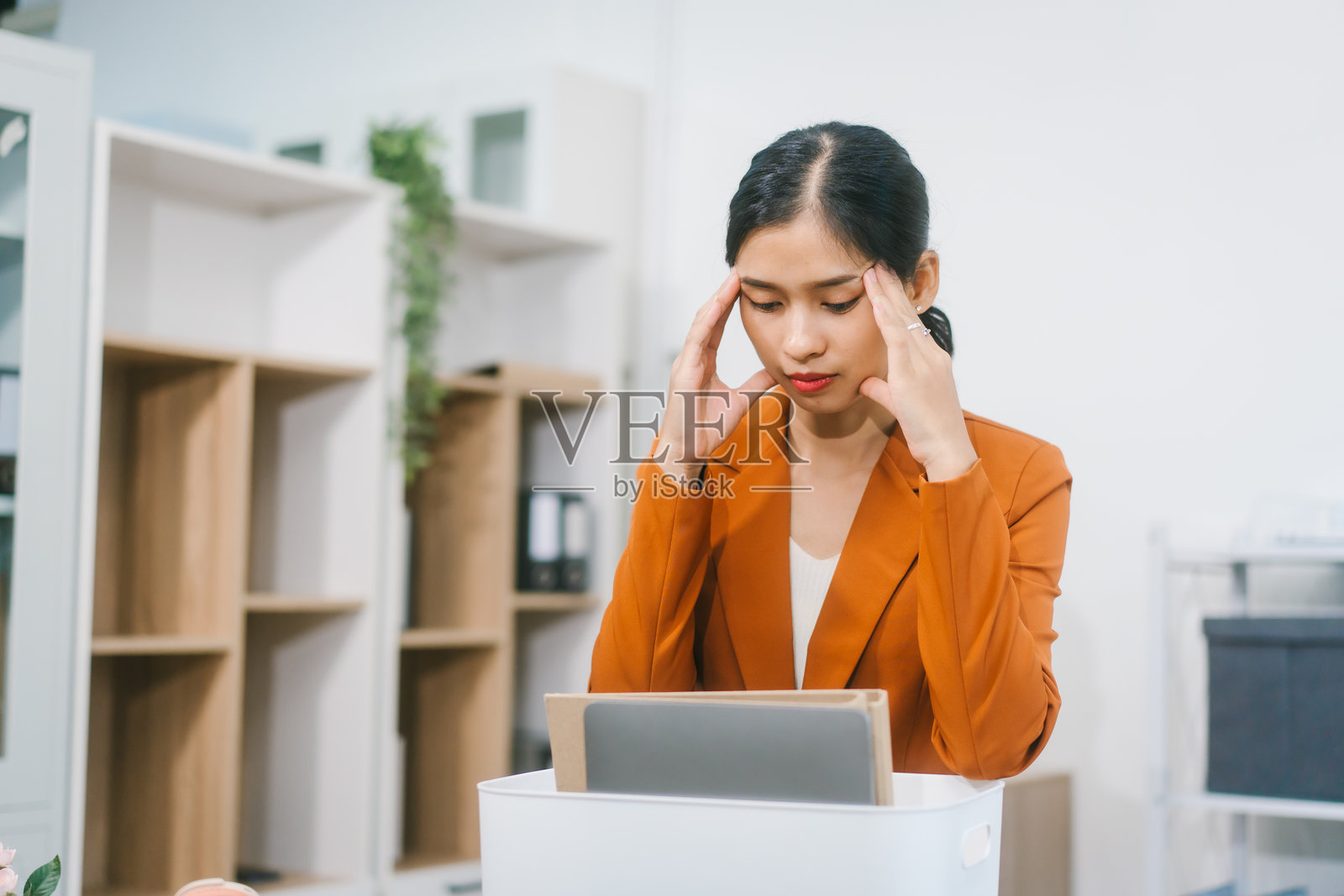 一位身着正装西装的年轻亚洲女性，自信而积极地将物品装入箱子，同时手持平板电脑，似乎为她的专业工作空间的转型做好了准备。照片摄影图片