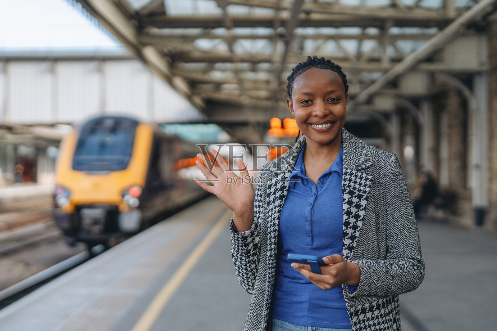 女子在火车到达前，一边使用手机一边在火车站挥手告别照片摄影图片
