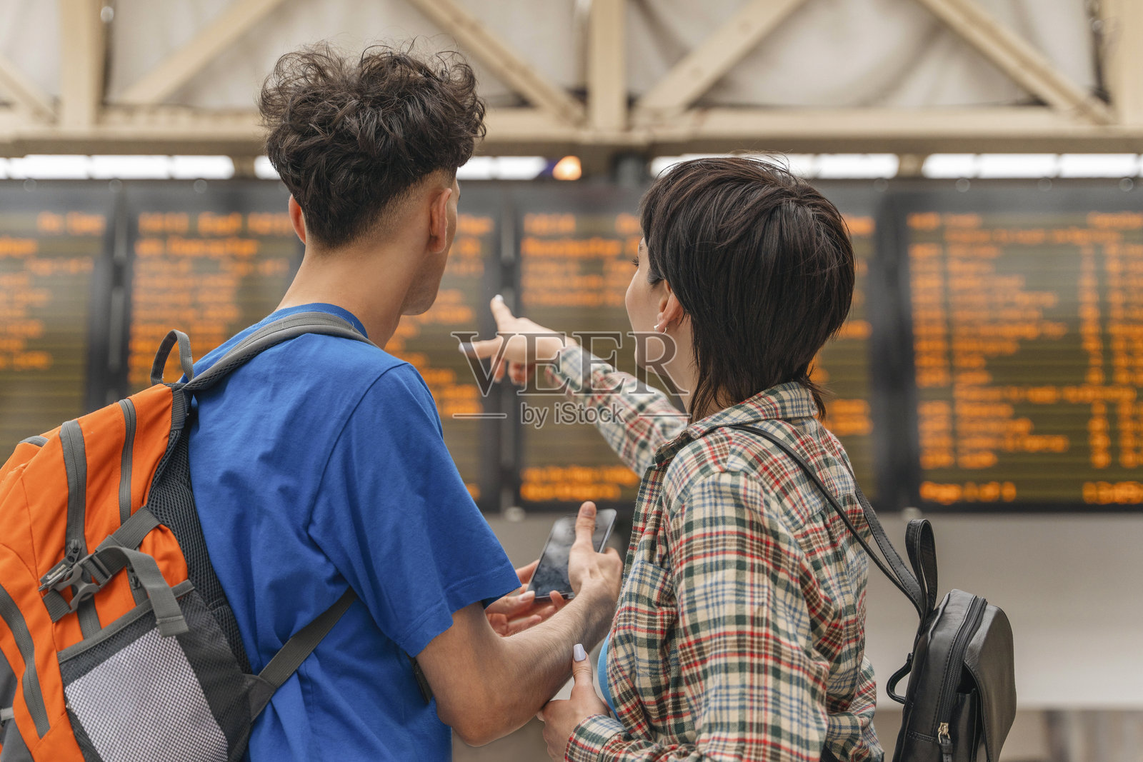 下午的阳光下，朋友们在火车站查看行程，可以看到出发指示牌。照片摄影图片