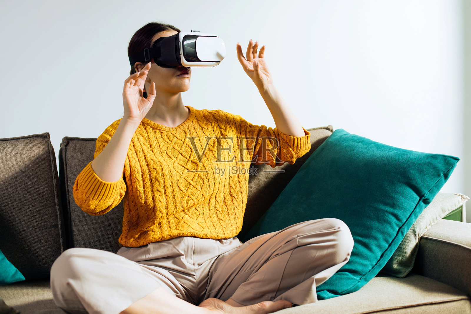 一名女子戴着虚拟现实头显，双手在空中挥动与视觉内容互动，她身处一个房间内，背景和墙壁都很简单明亮。照片摄影图片