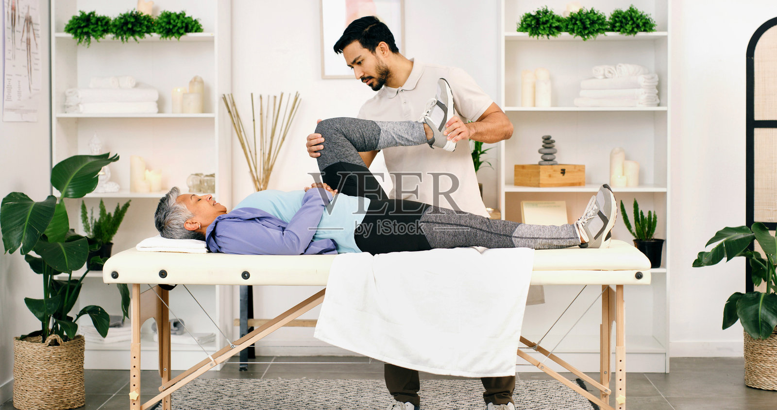 老年妇女在治疗台上伸展腿部接受理疗，医护人员协助其肌肉恢复与健康。老年人接受脊骨神经医生支持的锻炼和物理治疗，获得帮助和援助。照片摄影图片