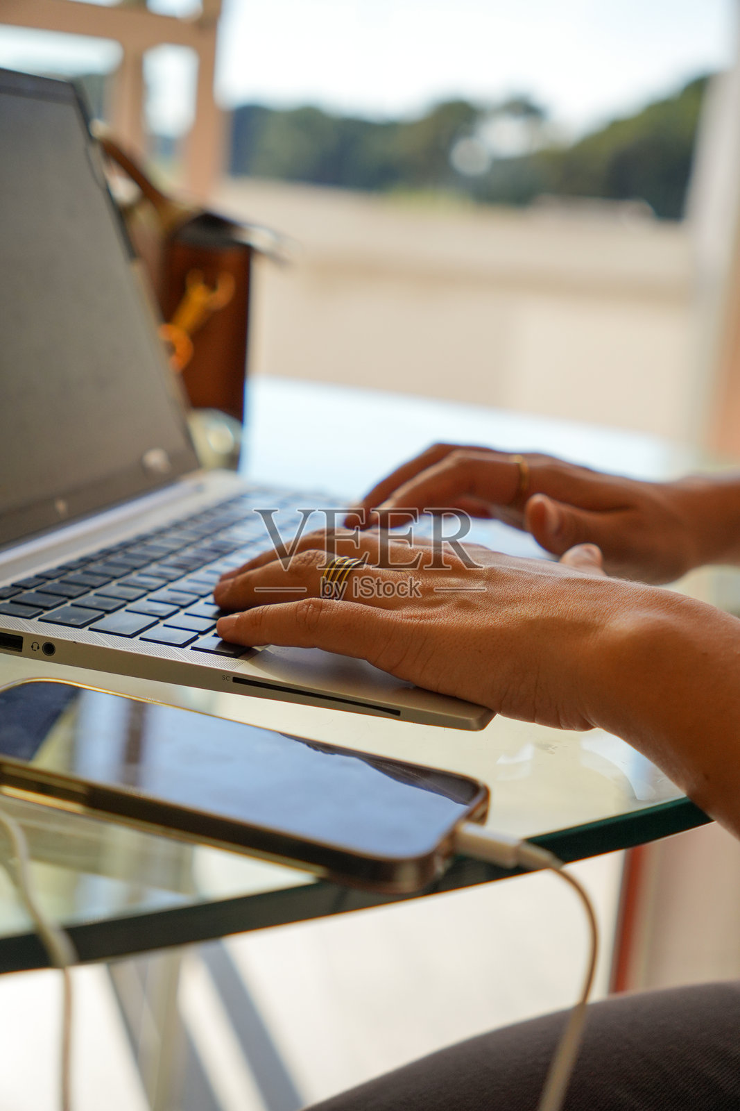 一位女士一边用笔记本电脑打字，一边拿着手机照片摄影图片