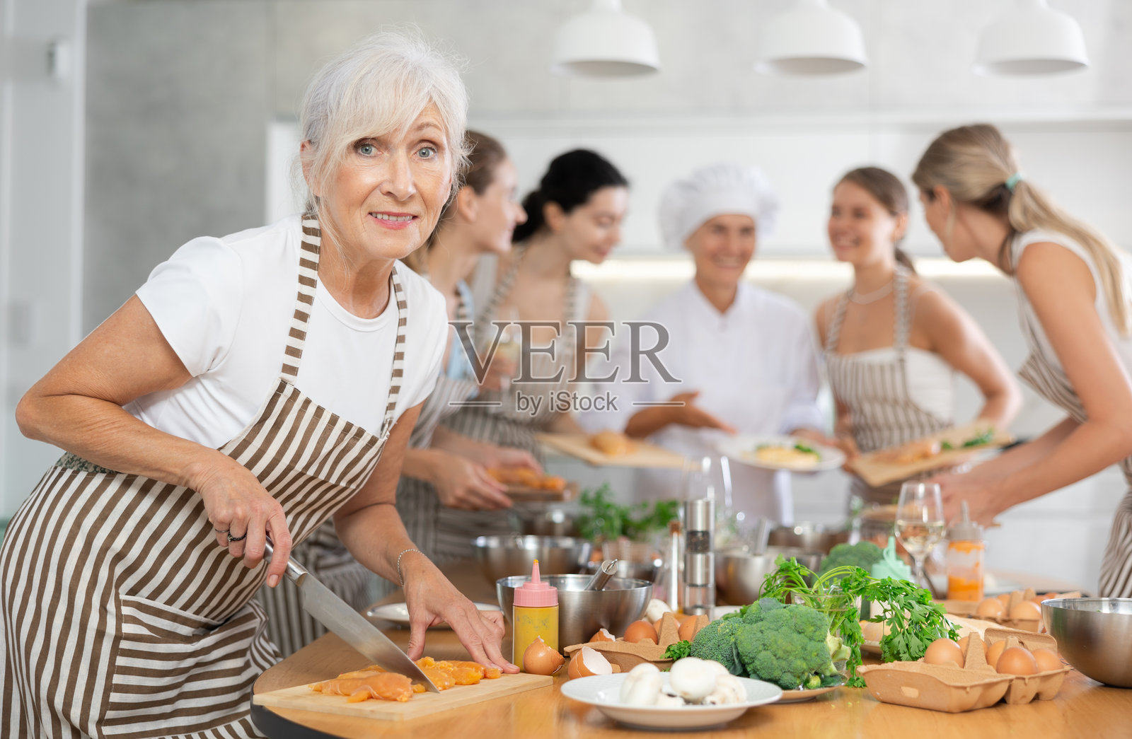 一位年长女性在烹饪学校的团体课程中，正在切鸡肉，准备低热量午餐照片摄影图片