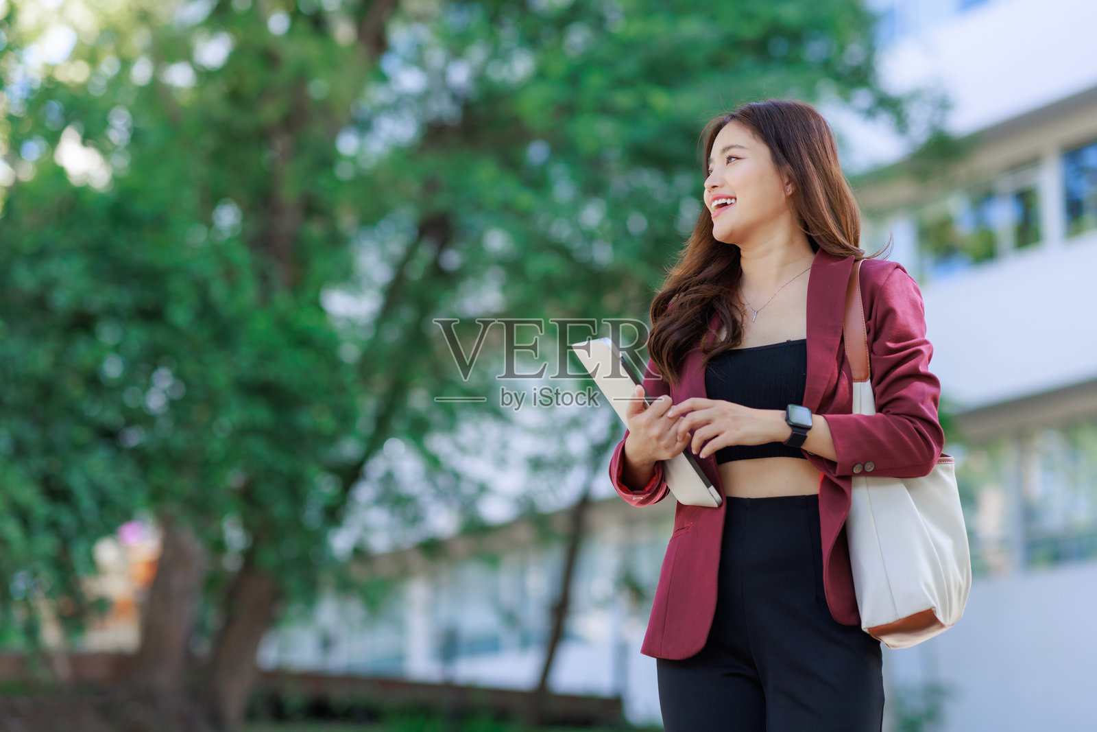 年轻的亚洲女性在户外行走，手持平板电脑，面带微笑照片摄影图片