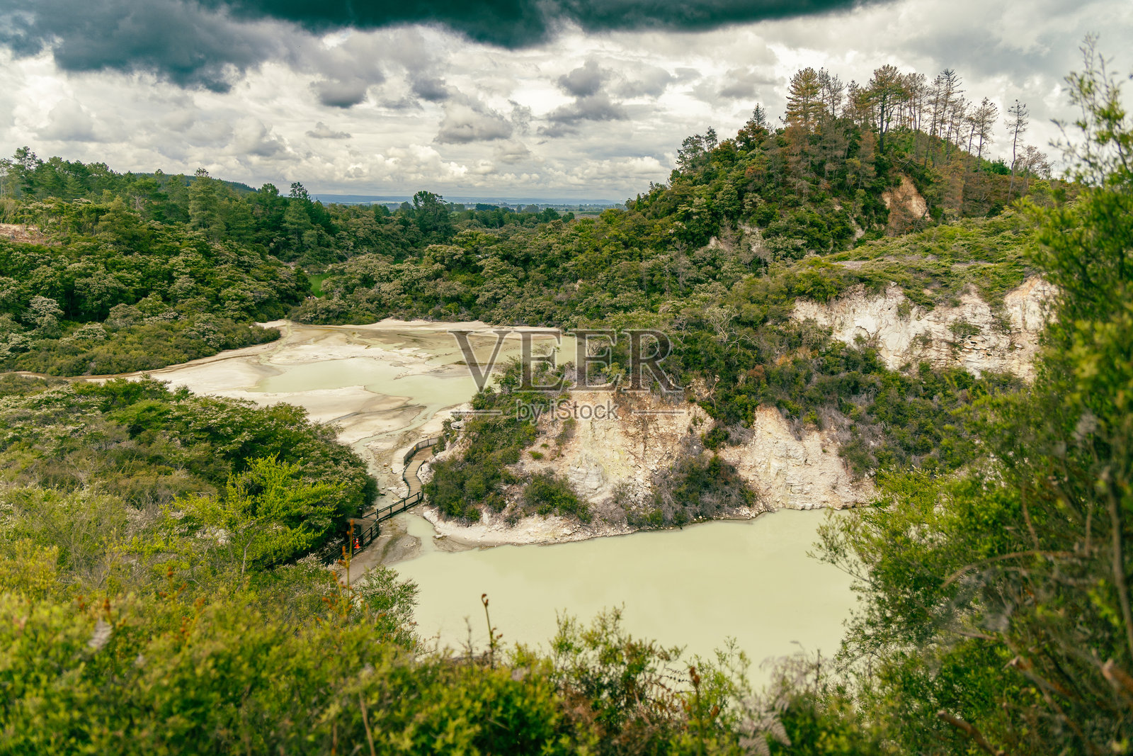 绿色森林覆盖的山丘，坐落于乳白色的地热湖上方照片摄影图片