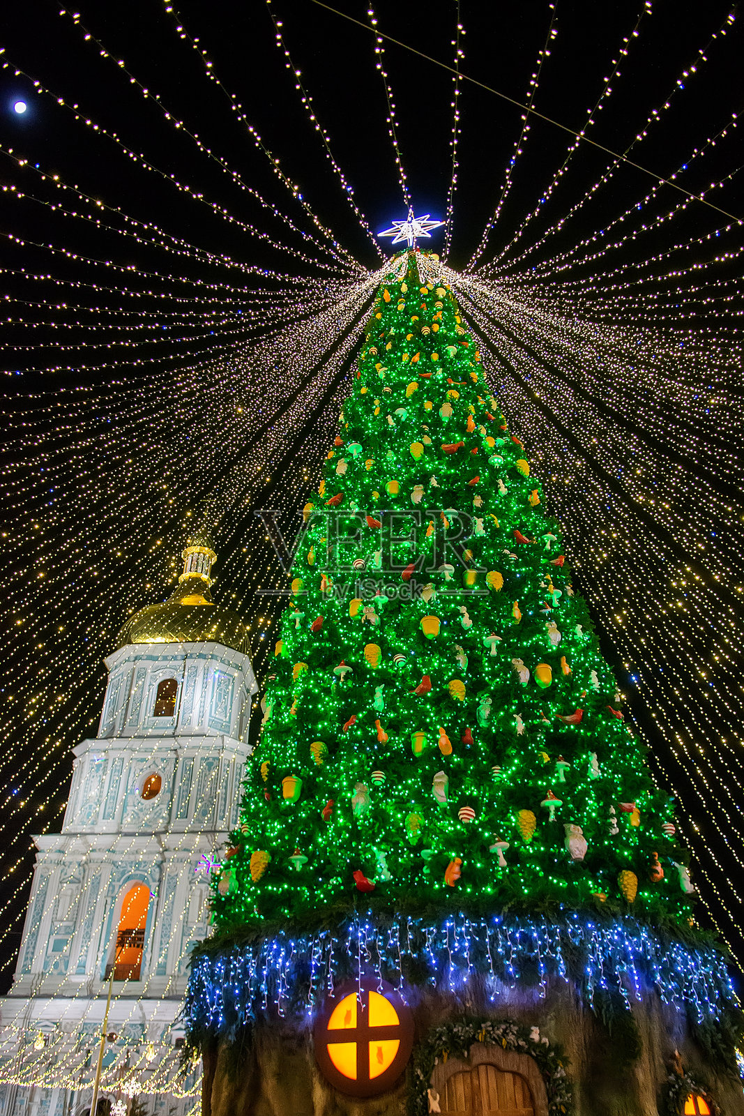 夜晚，巨大的装饰圣诞树在节日灯光的绚丽华盖下闪耀着绿色光芒，营造出欢乐的节日庆典氛围和神奇的冬日景象照片摄影图片