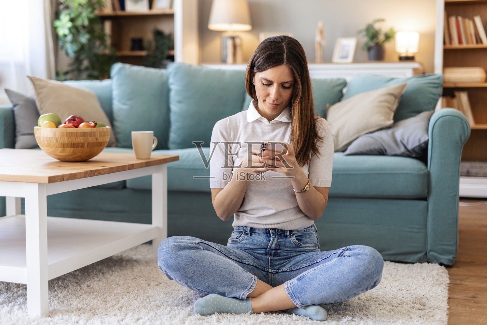 女人躺在地板上，边看手机边大笑，表情放松，内容涉及社交媒体和有趣的短信。这位女性在家中，使用手机，表情愉悦，适合迷因网站、搞笑视频和社交应用上的八卦闲聊。照片摄影图片