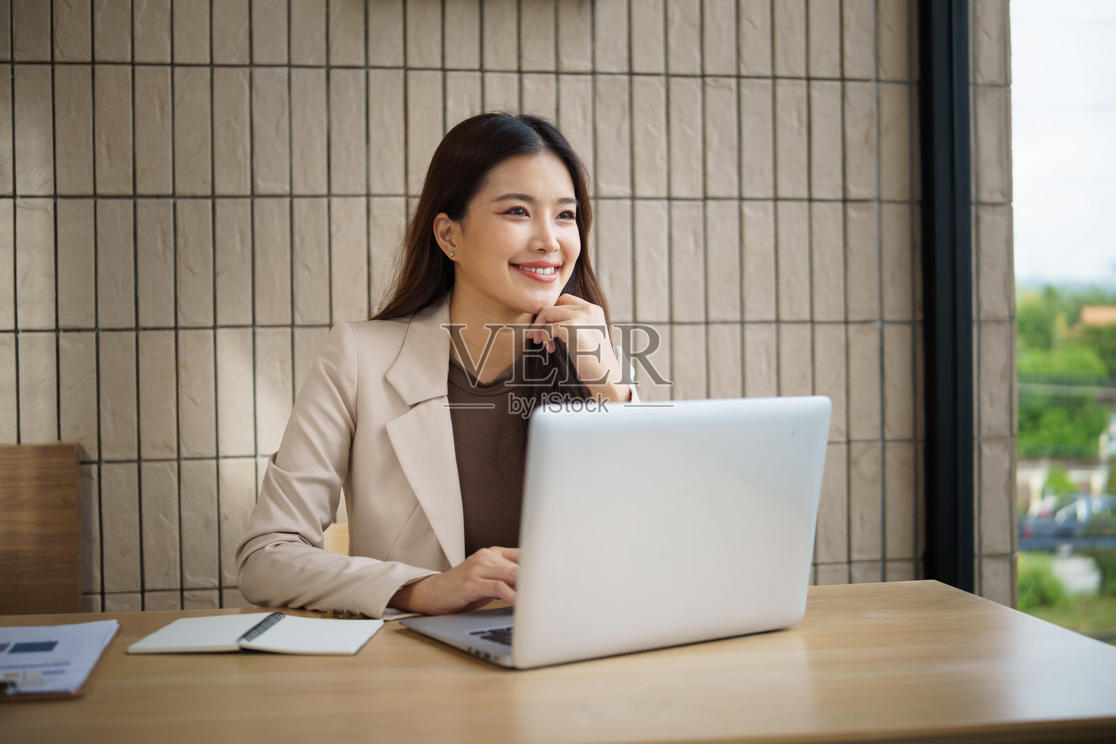 一位面带微笑的女商人在现代办公室环境中坐在办公桌前，看着笔记本电脑，显得灵感迸发。照片摄影图片