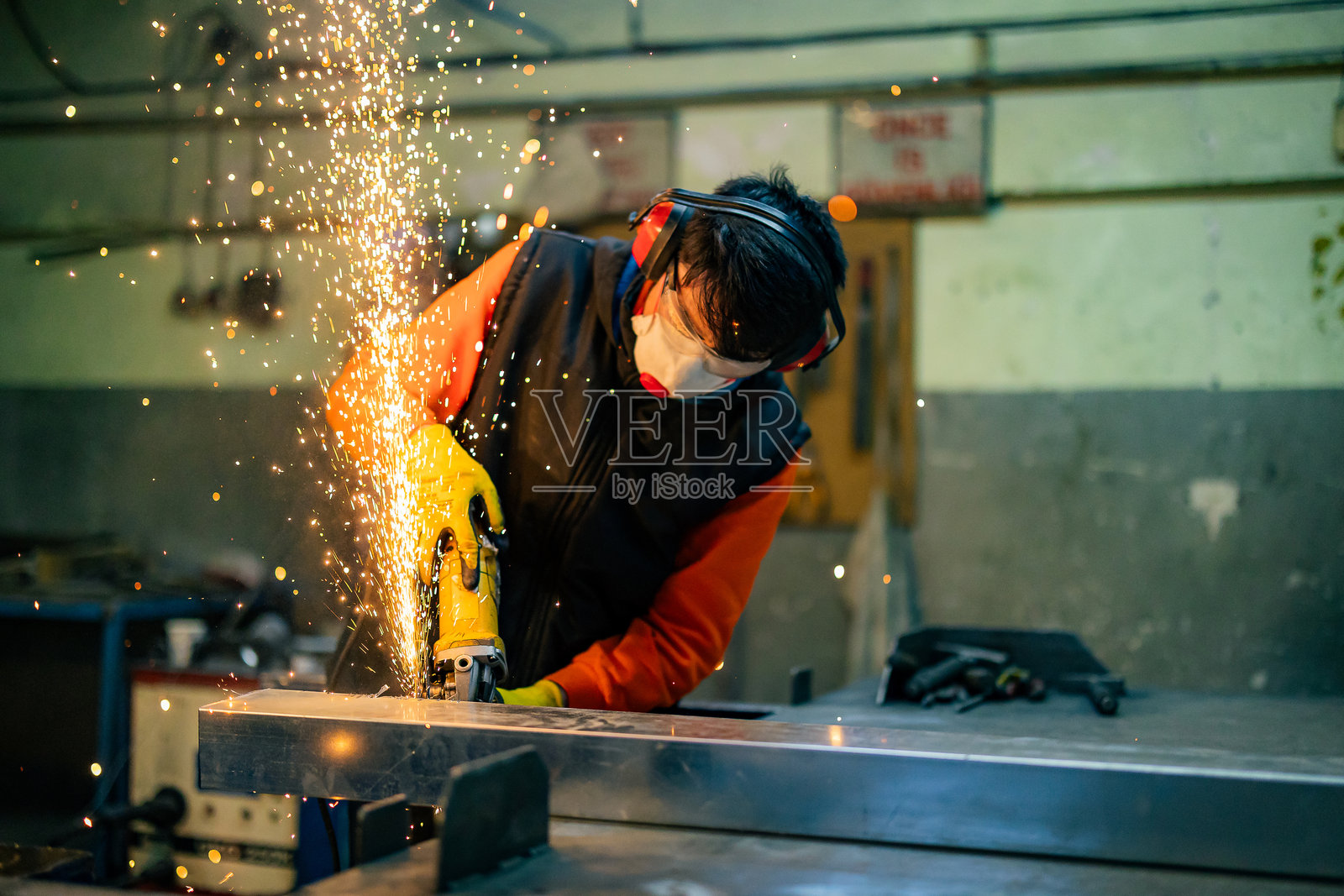 身着特制服装、佩戴护目镜的锁匠在生产中工作。使用角磨机进行金属加工。金属加工产生火花。照片摄影图片