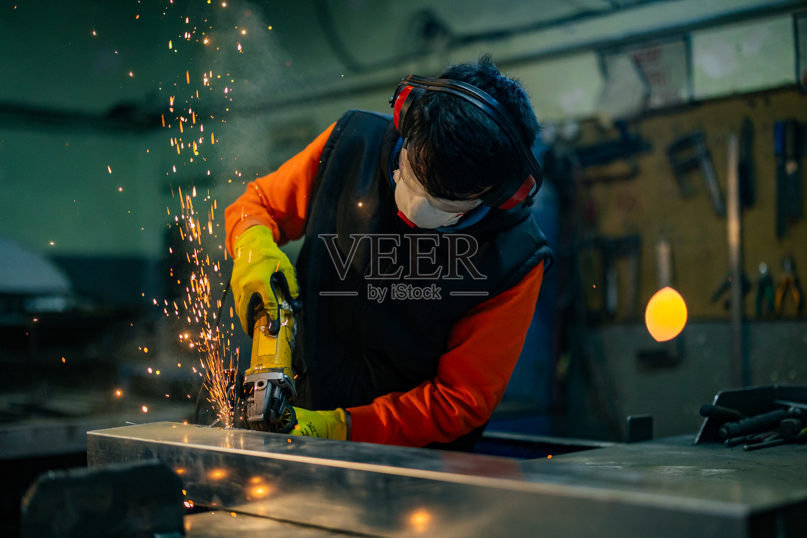 身着特殊服装、佩戴护目镜的锁匠在生产车间工作。使用角磨机进行金属加工。金属加工中的火花。照片摄影图片