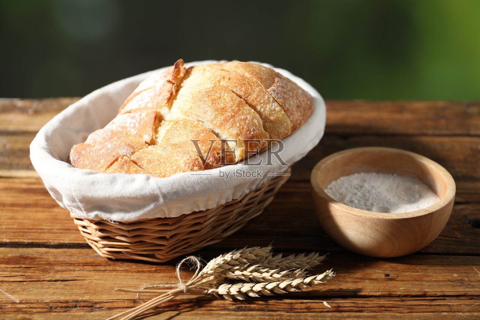 新鲜切面包放在柳条篮中，木桌上撒着面粉和麦穗，背景虚化，特写照片摄影图片