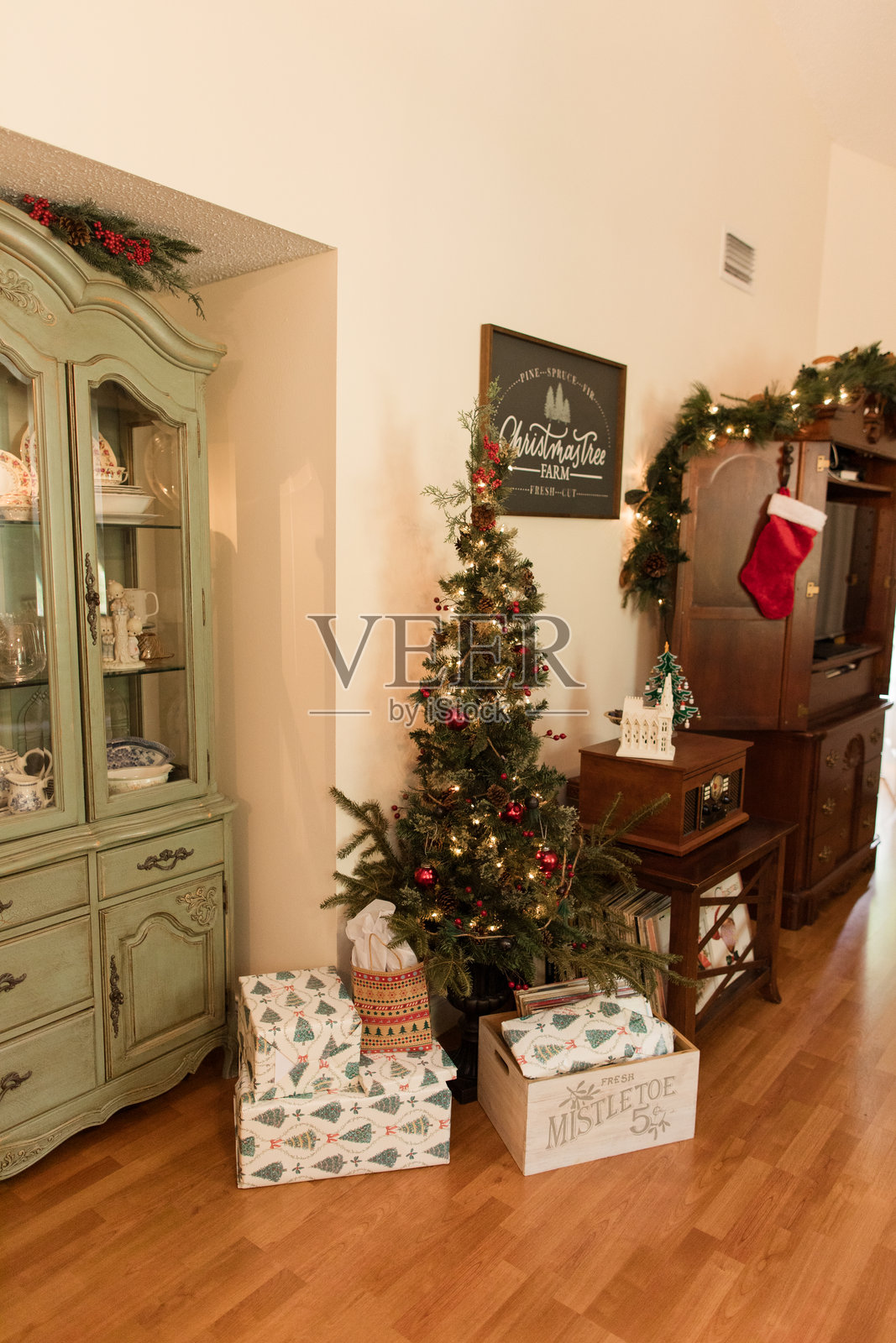 乡村复古鼠尾草绿餐边柜，摆放着传家古董，置身于舒适的乡村风格圣诞节小屋中，旁边是圣诞树和礼物照片摄影图片