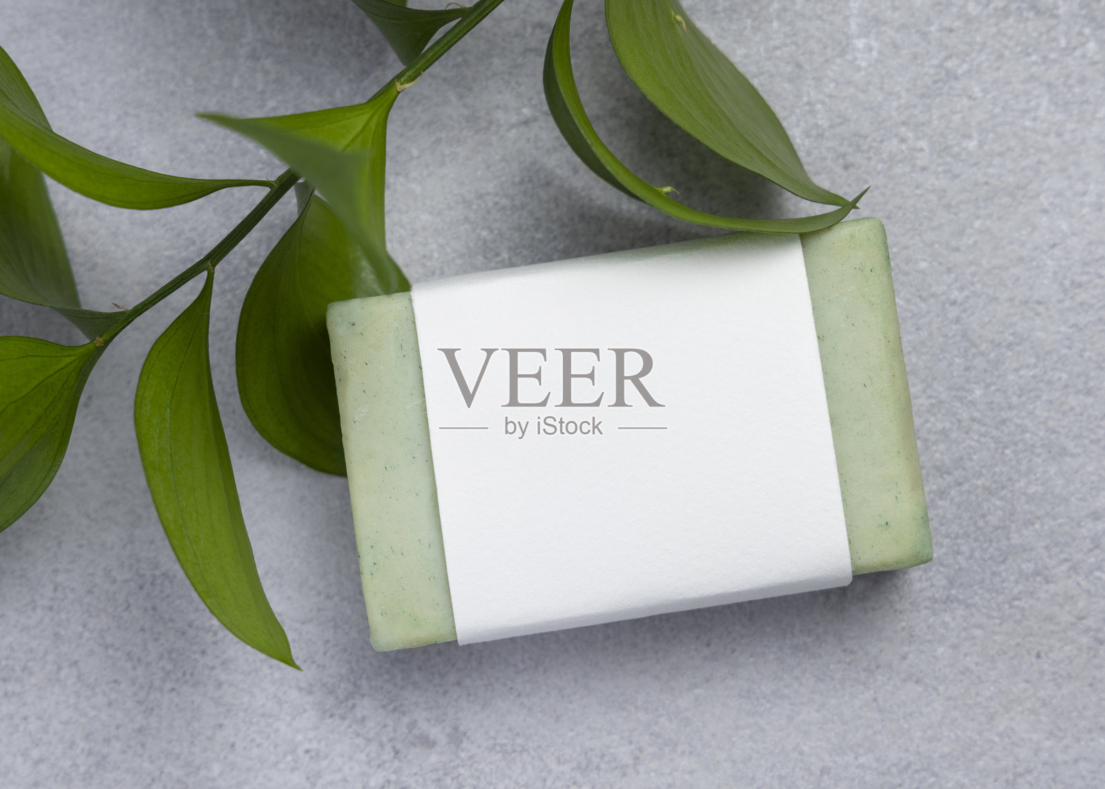 浅灰色石材台面上的肥皂，标签留白，旁边有绿色叶子和白色浴巾，俯视角度，样机照片摄影图片