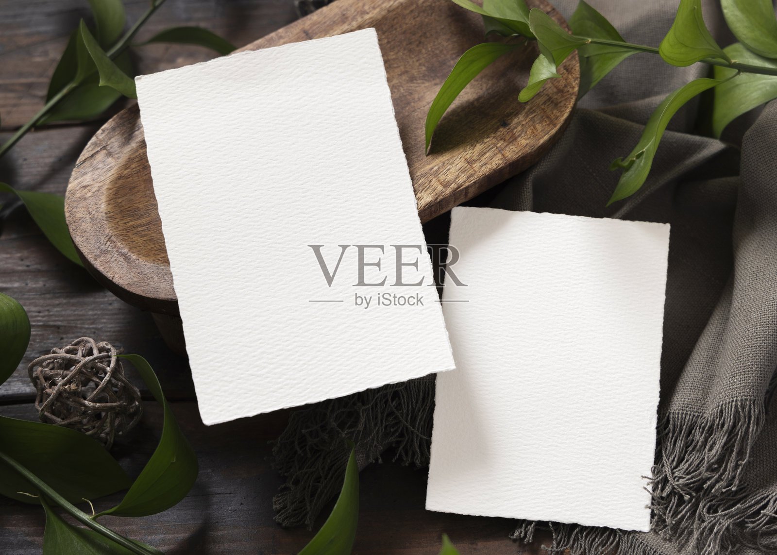 俯视视角，一张竖版卡片模型放在棕色木质托盘上，旁边有绿叶和灰色亚麻布照片摄影图片