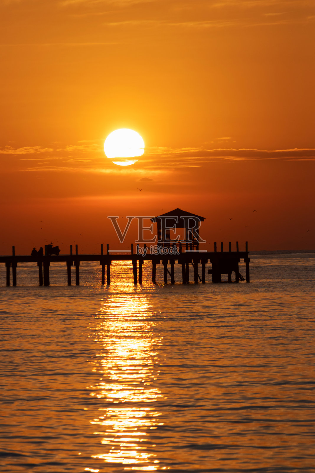 泰国สมุทรปราการ邦普金色的日落映照在平静的海面上，木制码头和凉亭的剪影反射着温暖的光芒。照片摄影图片