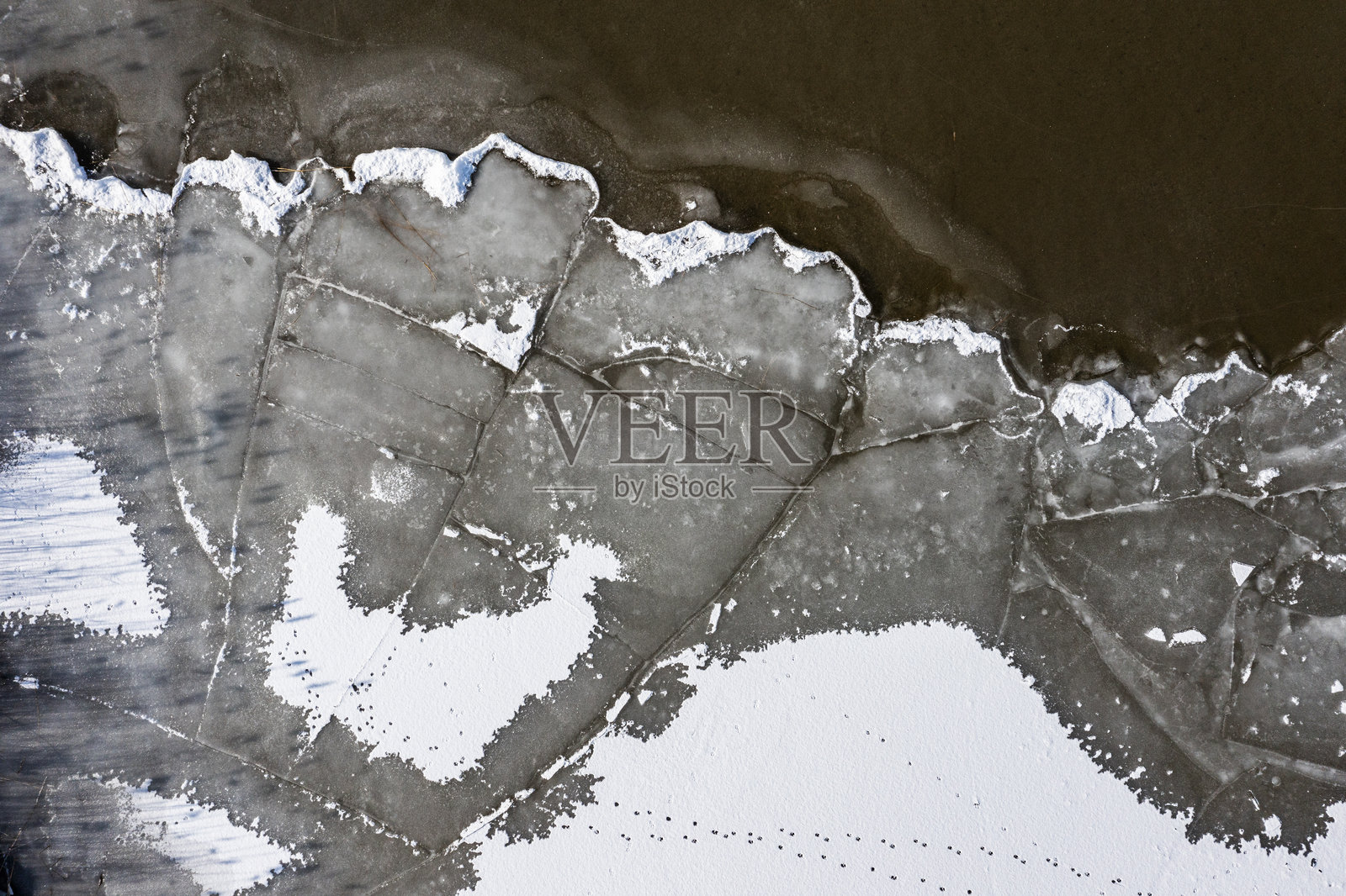 结冰湖泊的纹理和水中漂浮的冰块。无人机拍摄的冬季景观。照片摄影图片