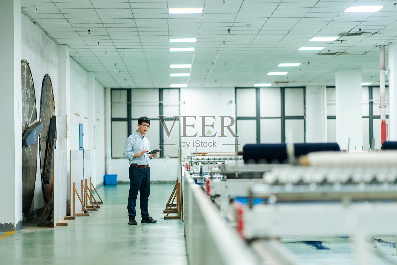 工厂车间内戴眼镜男性工程师手持平板巡查设备照片摄影图片