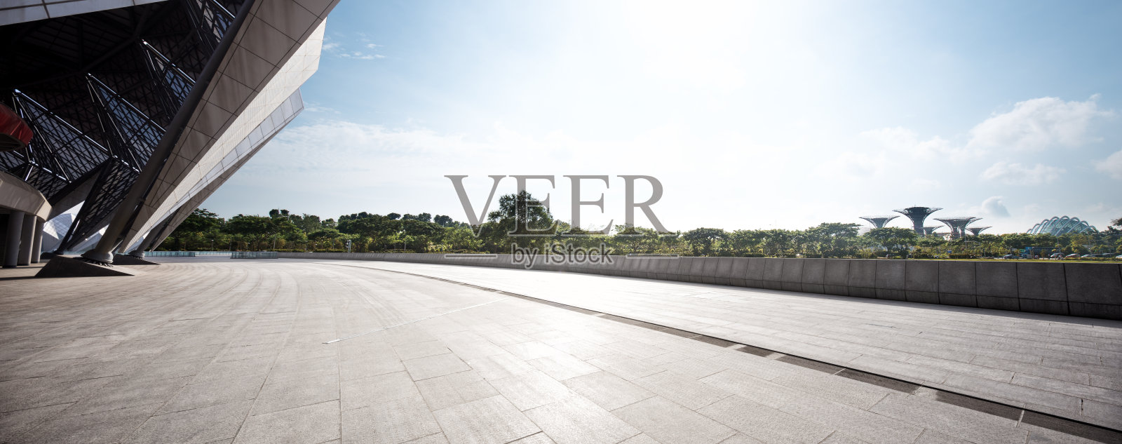 现代建筑广场空旷地面与远处绿植及超现实树状结构照片摄影图片