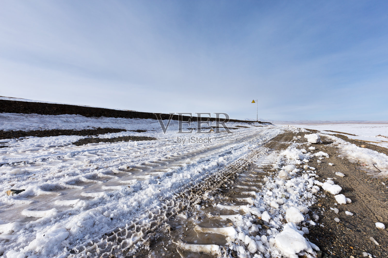 冰雪覆盖的冻土道路车辙痕迹与远处风力标志杆照片摄影图片
