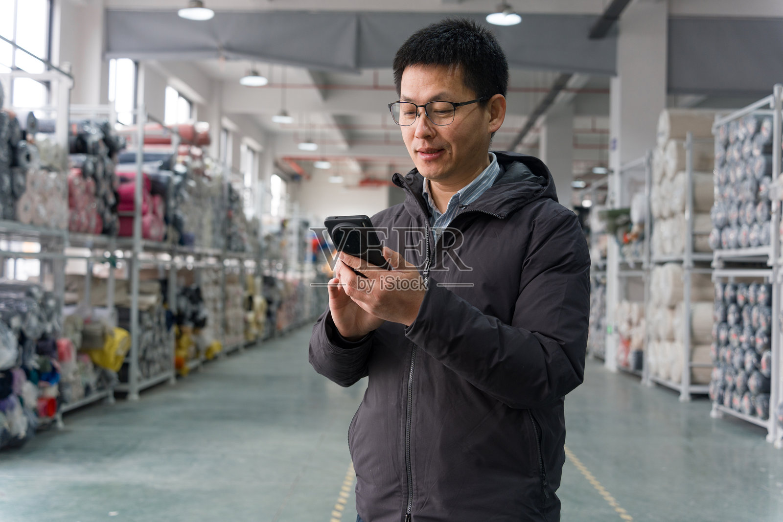 仓库中戴眼镜男子手持手机查看库存照片摄影图片