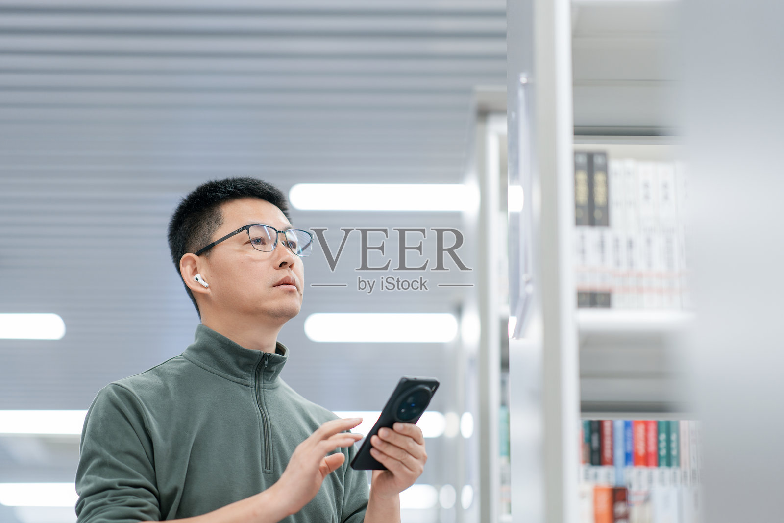 戴眼镜男子图书馆持手机查阅资料照片摄影图片