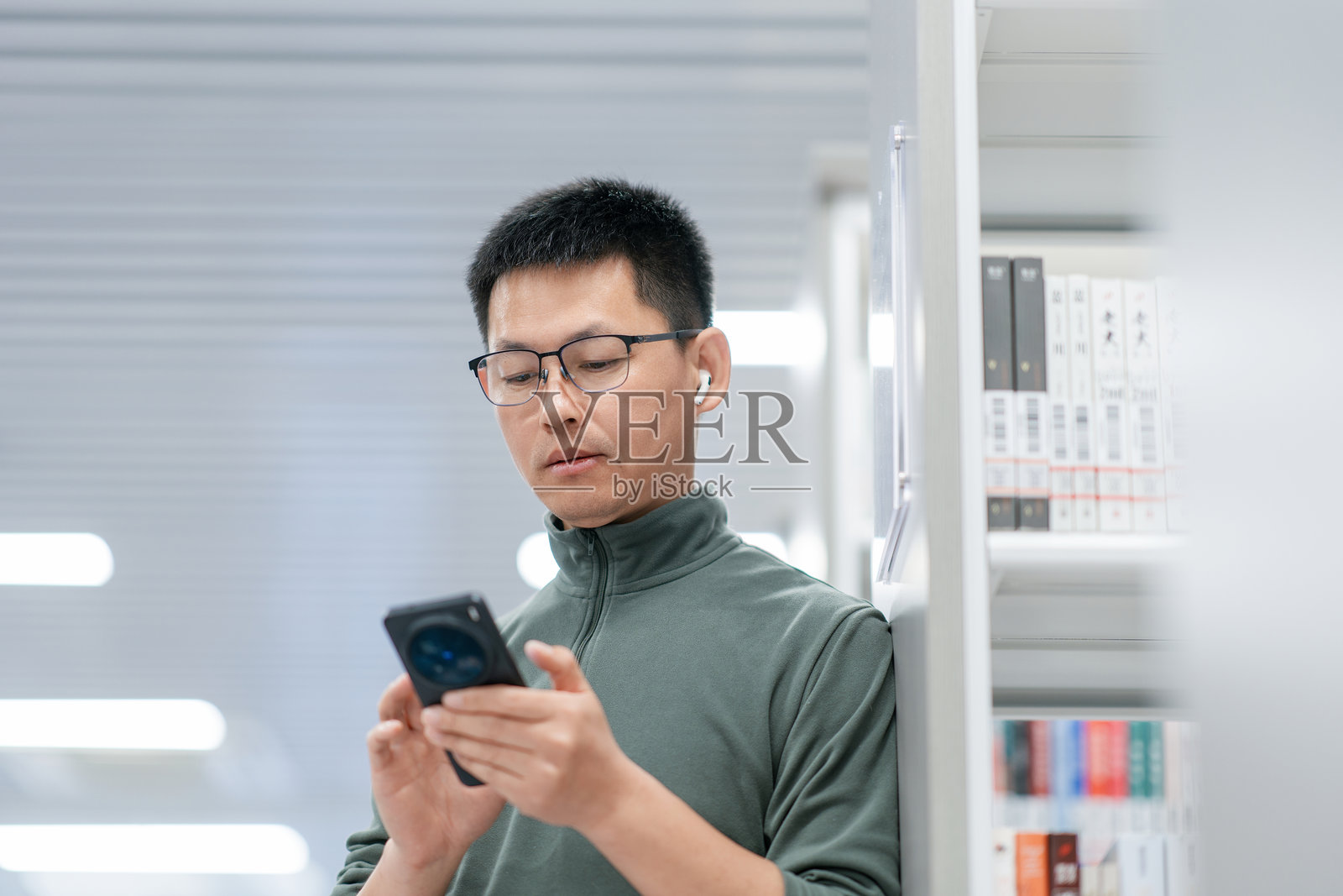 戴眼镜男子图书馆内专注看手机照片摄影图片