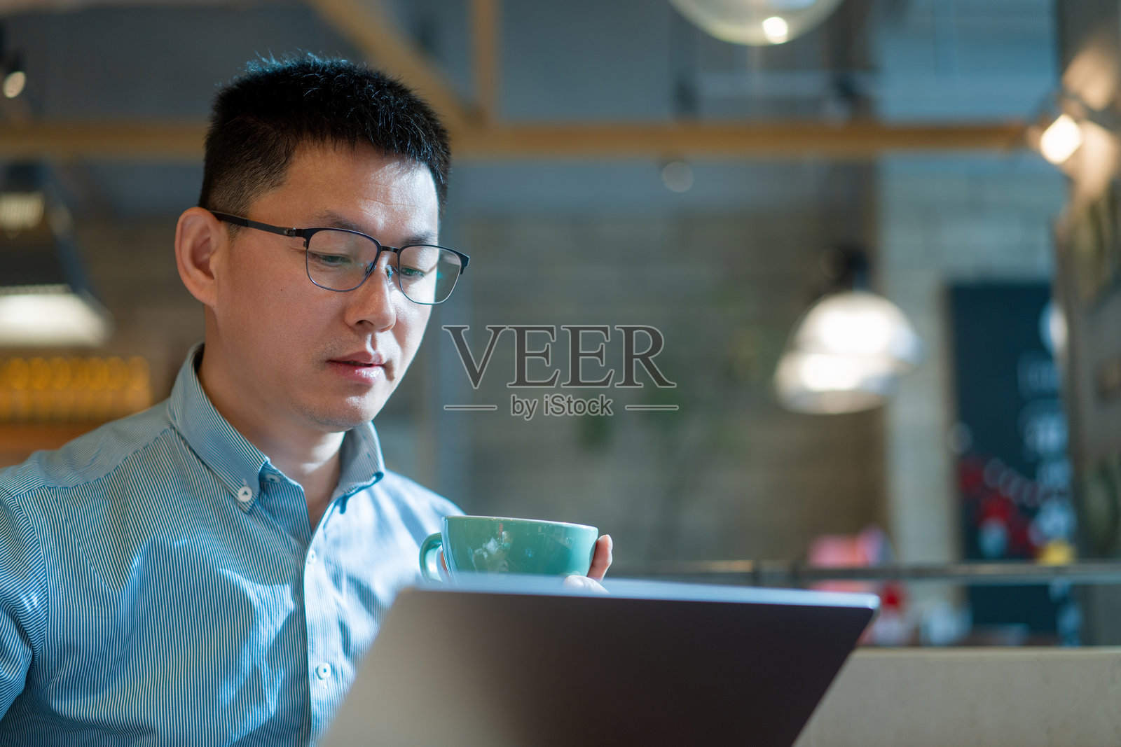 戴眼镜男子手持咖啡专注看笔记本照片摄影图片