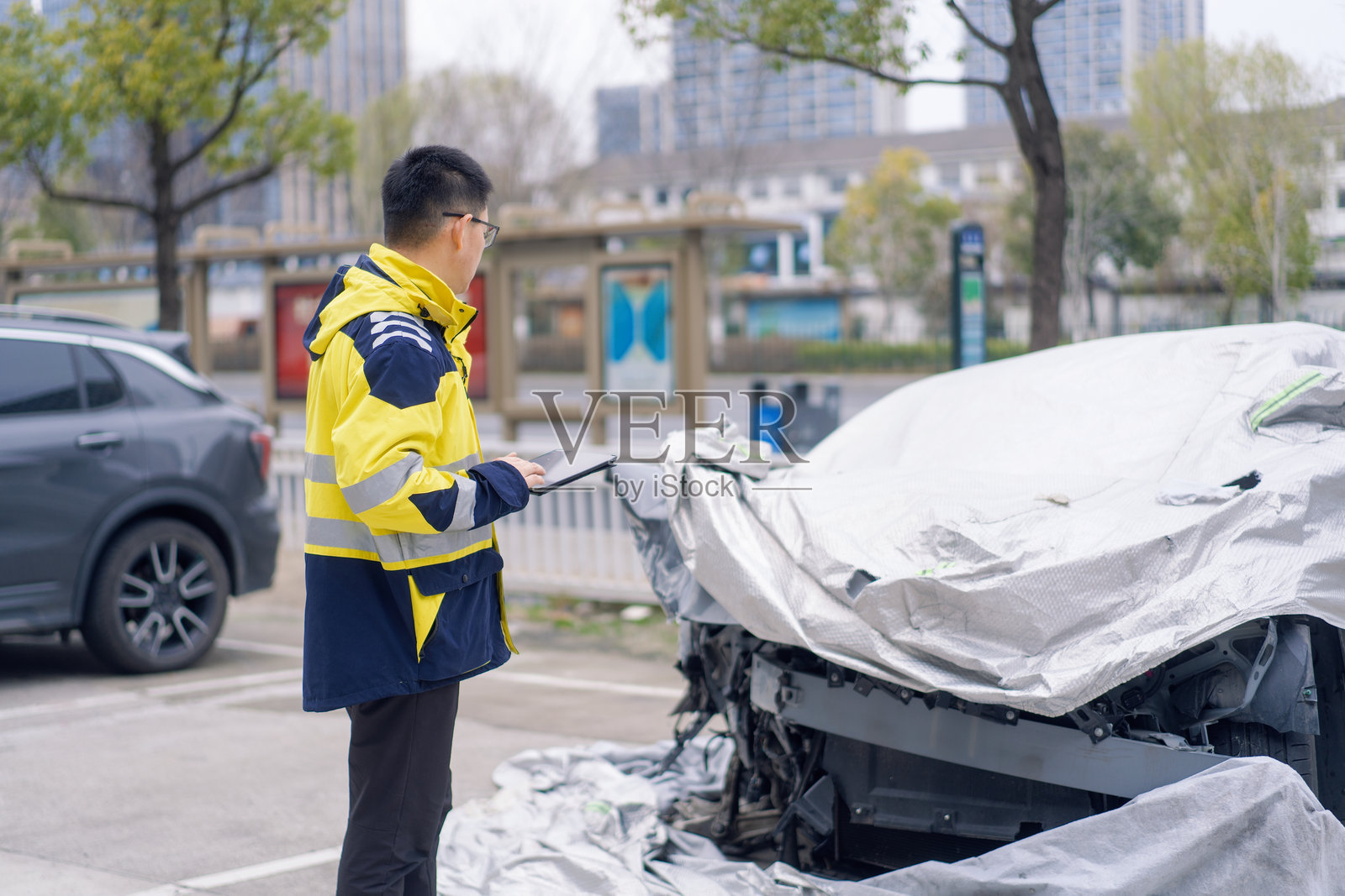 穿黄蓝反光服男子查看覆盖车衣事故车照片摄影图片